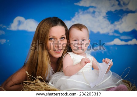 cheerful, kind, smiling child sitting her mother on the grass against the blue sky