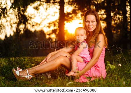 young beautiful woman sitting with a baby in a forest at sunset