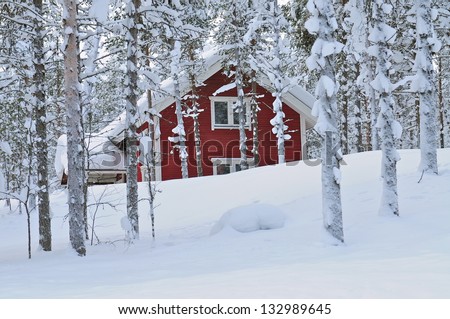 Snow covered log cabin between the trees in Lapland, Finland