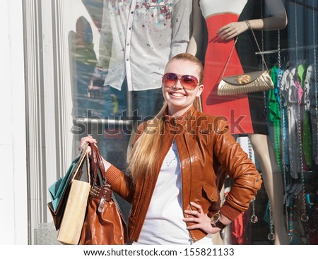 Portrait of lovely young woman smiling and carrying shopping bag near fashion shop