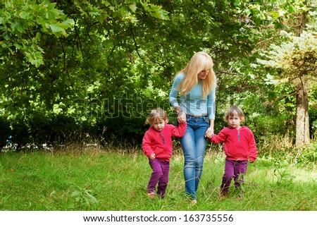 Picture of happy young family in park, cute mother with two sweet twins walking outdoors
