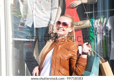 Portrait of lovely young woman smiling and carrying shopping bag near fashion shop