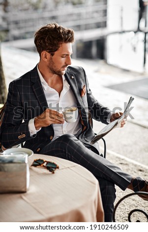 Handsome man drinking coffee and reading newspaper in cafe