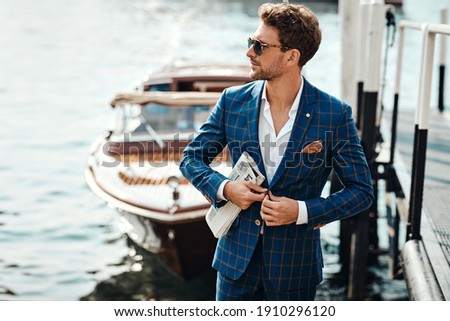 Young handsome man in classic suit over the blurred lake buttoning his jacket