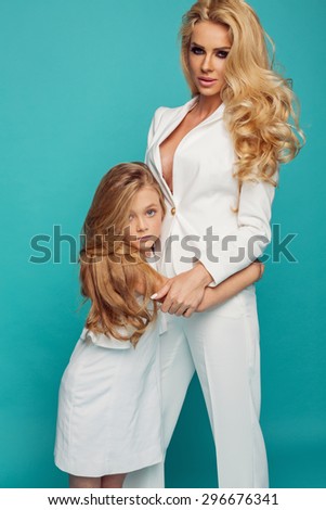 Fashion photo of beautiful mother and daughter in white clothes isolated on turquoise background