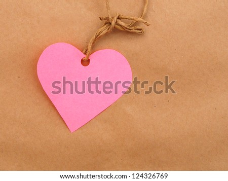 String tied in a bow with pink heart over brown paper packaging.