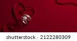 2 white gold engagement rings with diamonds and a heart-shaped ribbon on a red background. Romantic wedding jewelry background. 3d render illustration.