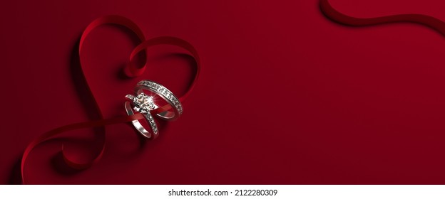 2 White Gold Engagement Rings With Diamonds And A Heart-shaped Ribbon On A Red Background. Romantic Wedding Jewelry Background. 3d Render Illustration.