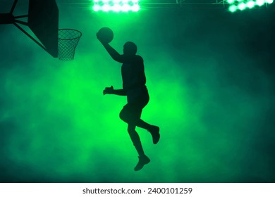 3d illustration shadow silhouette of professional basketball player layup on dark green smoke background - Powered by Shutterstock