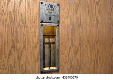 A 3D render of an empty illuminated vintage photo booths retrieval slot on a wood finished surface