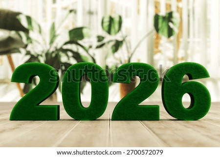 3D render of green grass numbers 2026 on a wooden floor with blurred houseplants in the background. No people. Eco style, natural theme, copy space.