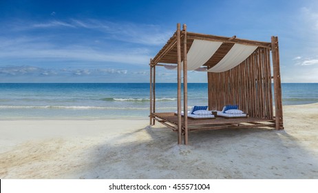 3D rendering image of bamboo tent which cover by fabric located on the beach,  fabric ceiling being blow by wind from the sea, white and blue day bed and pillow
