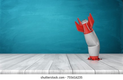 3d rendering of a red and silver realistic model of a retro rocket stands crashed into a wooden desk on a blue background. Failed launch. Technological progress. Technical mistake.