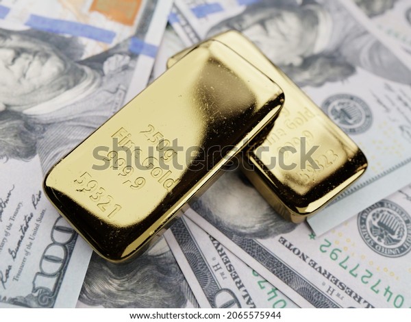 3D rendering of two 250g fine gold ingots placed\
on wads of 100 US\
dollars
