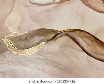 Abstract beige background with gold, beautiful smudges and stains made with alcohol ink and gold pigment. Fragment of art with beige texture resembles marble, watercolor or aquarelle painting.
