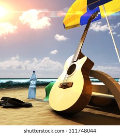 Acoustic Guitar Near The Deck Chair Under Umbrella On The Beach At Sunset