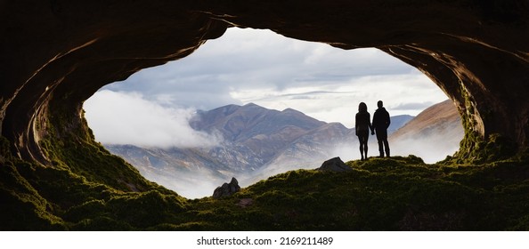 Adventurous Man and Woman Couple standing in a rocky cave. Mountain Nature Landscape with clouds in background. Sunny Sunrise or Sunset. 3d Rendering Adventure Art. - Powered by Shutterstock