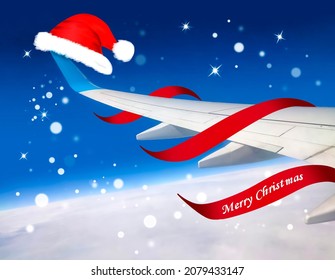 Airplane with red Santa Christmas hat over clouds and blue sky. Christmas happy travel and vacation concept.