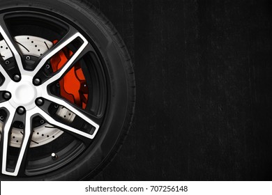 Alloy wheels of racing car with metal brake discs and red caliper on a black cement wall background with copy space your writing text on the right. Automotive parts concept.