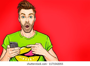 Attractive Amazed Young Man Pointing Finger On Mobile Phone In Comic Style. Pop Art Surprised Guy Holding Smartphone. 