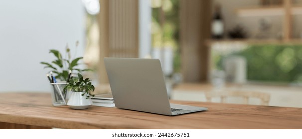 A back view image of a laptop computer on a wooden dining table in a neutral contemporary dining room or kitchen. home workspace concept. 3d render, 3d illustration