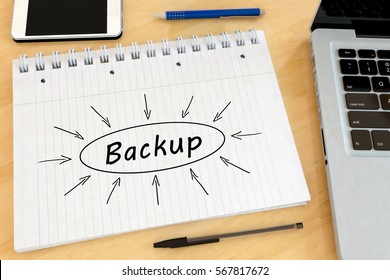 Backup - handwritten text in a notebook on a desk with laptop and mobilephone- 3d render illustration.