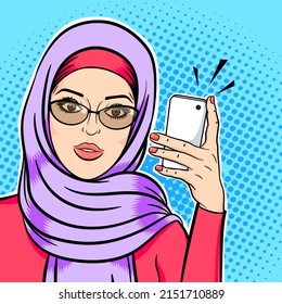 Beautiful muslim woman in hijab holding mobile phone reading sms or taking selfie concept in pop art comic retro style.