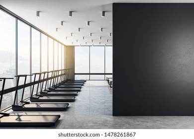 Big Blank Black Wall In A Modern Gym With Fashion Treadmills, Concrete Floor And Big Clean Windows In A Skyscraper. Health Concept. 3D Rendering