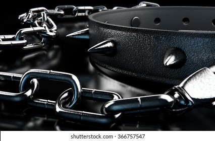 A black leather dog collar with metal spiked studs attached to a metal chain isolated on a dark studio background