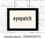 Black wooden frame with inscription eyepatch hanging on white brick wall 