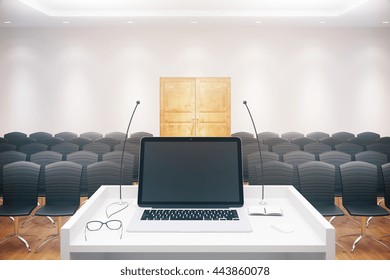 Blank Laptop Placed On Speaker's Stand In Conference Hall Interior With Rows Of Seats And Wooden Door. Mock Up, 3D Rendering