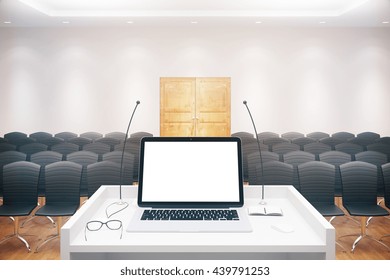 Blank White Laptop Placed On Speaker's Stand In Conference Hall Interior With Rows Of Seats And Wooden Door. Mock Up, 3D Rendering