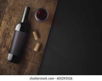 Bottle of red wine with label on old board. Glass of wine and cork. Wine bottle mockup. Top view.