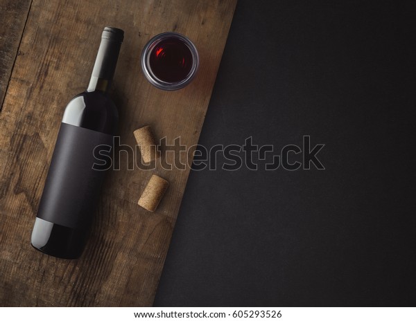 Bottle of red wine with label on\
old board. Glass of wine and cork. Wine bottle mockup. Top\
view.