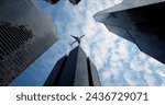 Bottom view of a passenger long-haul aircraft liner flying over skyscrapers in the business center of a large city. Reflections of the plane in the windows of buildings on a sunny day. Travel concept.