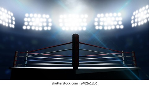 An boxing ring surrounded by ropes spotlit by floodlights in an arena setting at night
