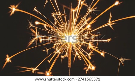 A bright sparkler emits a dazzling array of golden sparks and light against a dark, contrasting background, creating a festive and celebratory atmosphere.