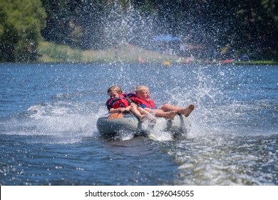 Children Tubing Behind Boat On An Inflatable Tube.