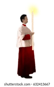 Christian catholic altar boy or server in red cassock and white surplice, carrying a lit candle