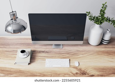 Close up of designer office interior with various objects, coffee cup and empty mock up place on computer monitor. Wooden desktop. 3D Rendering