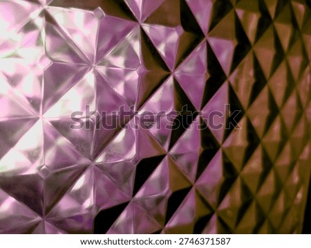 Close up of a translucent glass block wall featuring a repetitive 3D diamond and triangle geometric pattern. Vibrant polychromatic gradient colors of purple, pink, and gold are illuminated by light refraction and internal reflection, creating a high-contrast prismatic effect