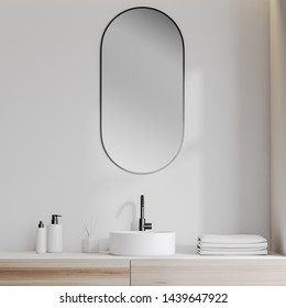 Close Up Of White Bathroom Sink Standing On Wooden Counter With Oblong Mirror Above It In Room With White Walls. 3d Rendering