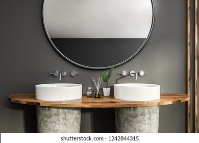 Close Up Of White And Stone Double Bathroom Sink Standing On Wooden Shelf In Room With Gray Walls And Large Round Mirror. 3d Rendering