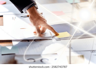 Close-up of a hand pointing at documents on a desk, surrounded by papers and notes, indicating a business or office setting with a focus on organization.
