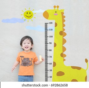 Closeup Happy Asian Kid Stand For Measure Height With Cute Cartoon At The Marble Stone Wall Textured Background