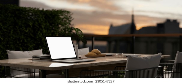 Close-up image of a laptop computer white screen mockup on an outdoor dining table in a beautiful restaurant with beautiful city view. 3d render, 3d illustration