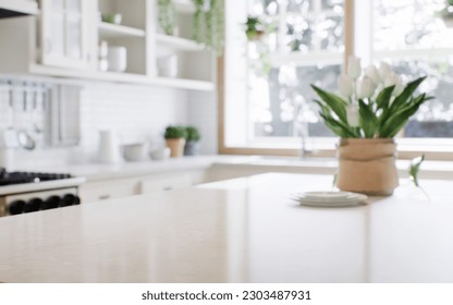 Close-up of a marble countertop of an island kitchen against a blurred background of a kitchen with appliances and utensils by a window with a green plant. 3d rendering
