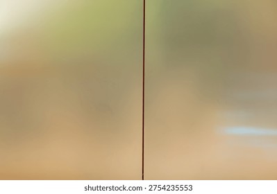 a close-up view of glass panel. The glass has a smooth, reflective surface with a blurred, warm-toned background of green, orange, and brown hues.