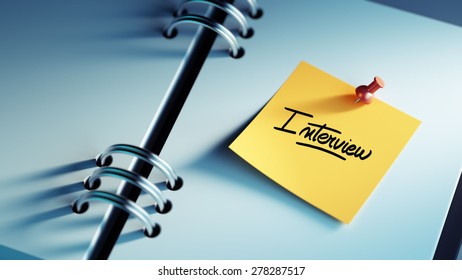 Closeup Yellow Sticky Note paste it in a notebook setting an appointment. The words Interview written on a white notebook to remind you an important appointment.