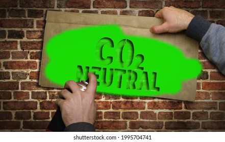 CO2 Neutral Climate, Environment And Ecology Crisis Spray Painted Inscription On The Brick Wall. Urban Abstract Concept Artwork. Airbrush Paint With Text Template In Hand.